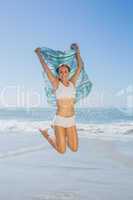 Gorgeous fit blonde jumping by the sea with scarf