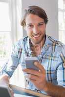Smiling casual man using laptop and texting on smartphone
