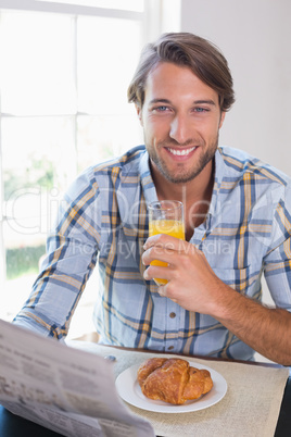 Casual smiling man having orange juice while reading newspaper