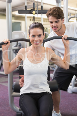 Fit brunette using weights machine for arms with trainer helping