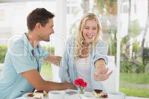 Hip young couple sitting at table admiring engagement ring
