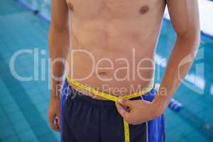 Fit man in swimming trunks standing by the pool measuring his wa
