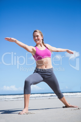 Happy fit blonde standing in warrior position on the beach