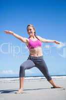 Happy fit blonde standing in warrior position on the beach