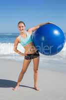 Fit woman standing on the beach holding exercise ball