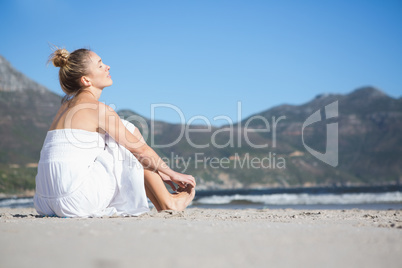 Content blonde in white dress sitting on the beach