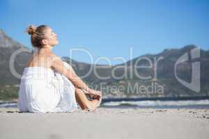 Content blonde in white dress sitting on the beach