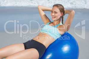 Fit woman lying on exercise ball at the beach doing sit ups