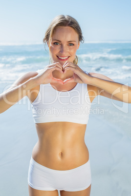 Gorgeous fit blonde making heart shape with hands by the sea