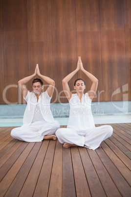 Attractive couple in white sitting in lotus pose with hands toge