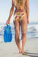 Woman holding flippers walking towards the sea