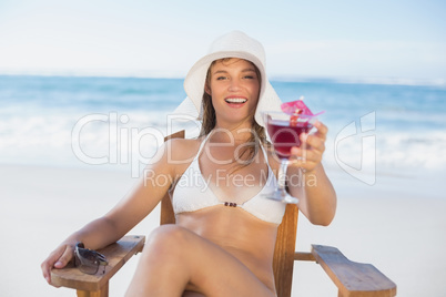 Pretty smiling blonde relaxing in deck chair on the beach with c