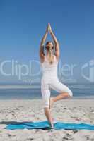 Blonde woman standing in tree pose on beach