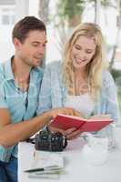 Cute hipster couple reading book together at table