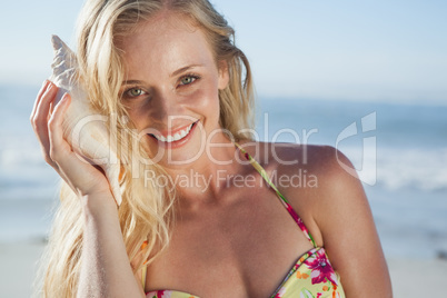 Pretty blonde in bikini listening to conch on the beach