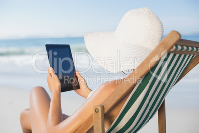 Woman relaxing in deck chair on the beach using tablet