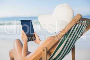 Woman relaxing in deck chair on the beach using tablet