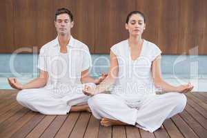 Attractive couple in white meditating in lotus pose