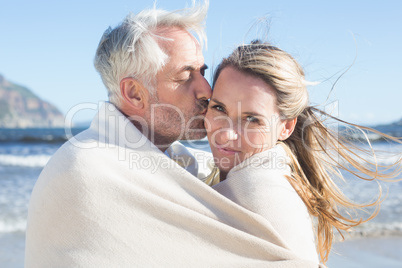 Smiling couple wrapped up in blanket on the beach