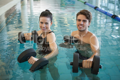 Man and woman standing with foam dumbbells in the pool