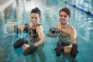 Man and woman standing with foam dumbbells in the pool