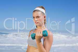 Sporty focused blonde lifting dumbbell on the beach