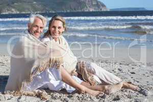 Smiling couple sitting on the beach under blanket