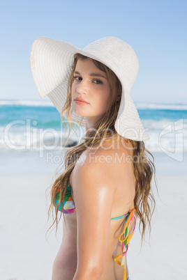 Beautiful girl on the beach posing in white straw hat and bikini