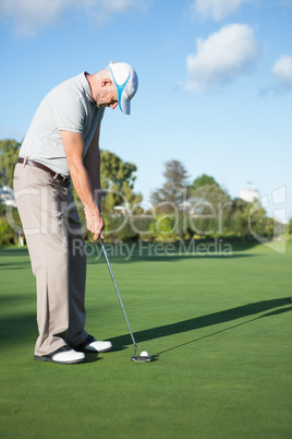 Handsome golfer putting ball on the green