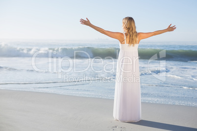 Blonde standing at the beach in white sundress with arms out