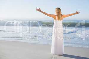 Blonde standing at the beach in white sundress with arms out
