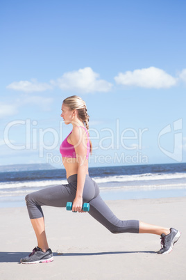 Fit woman working out with dumbbells on the beach lunging