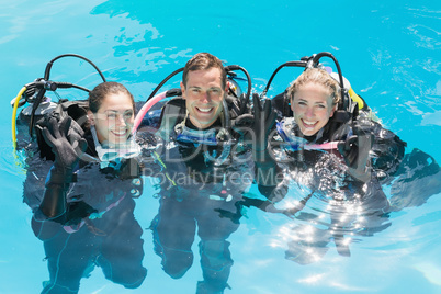 Smiling friends on scuba training in swimming pool looking at ca
