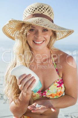 Pretty blonde sitting on the beach applying suncream