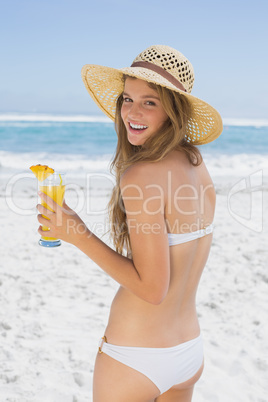 Smiling blonde in bikini holding cocktail on the beach