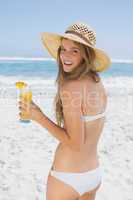 Smiling blonde in bikini holding cocktail on the beach