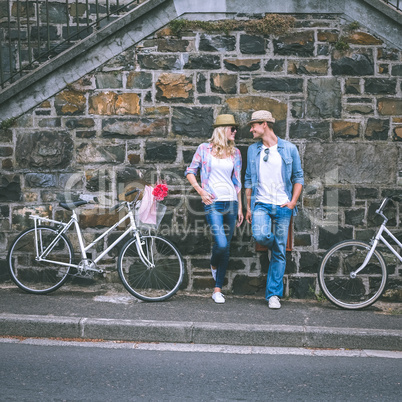 Hip young couple standing by brick wall with their bikes