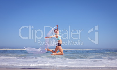 Fit woman jumping gracefully on the beach with scarf