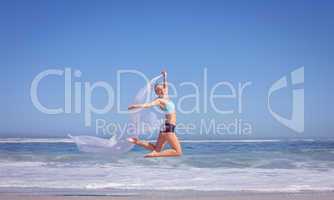 Fit woman jumping gracefully on the beach with scarf