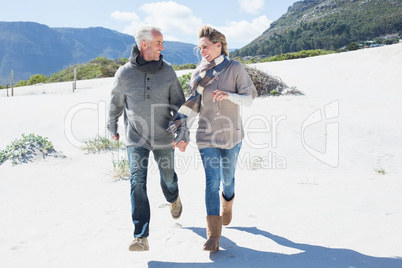 Smiling couple skipping on the beach in warm clothing