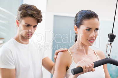 Fit smiling woman using weights machine for arms with her traine