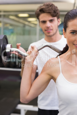 Fit smiling woman lifting barbell with her trainer