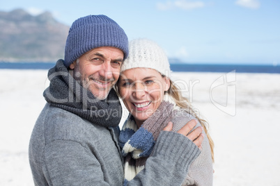 Attractive couple smiling at camera on the beach in warm clothin