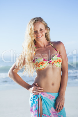 Pretty blonde in bikini and sarong smiling at camera on the beac