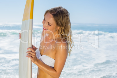 Smiling blonde surfer in white bikini holding her board on the b