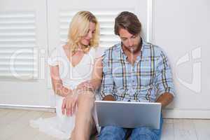 Cute young couple sitting on floor using laptop