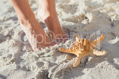 Woman standing beside starfish on the beach