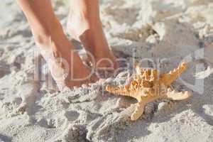 Woman standing beside starfish on the beach