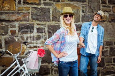 Hip young couple standing by brick wall with their bikes