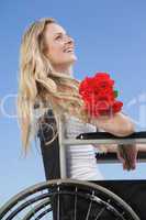 Wheelchair bound blonde smiling on the beach holding roses